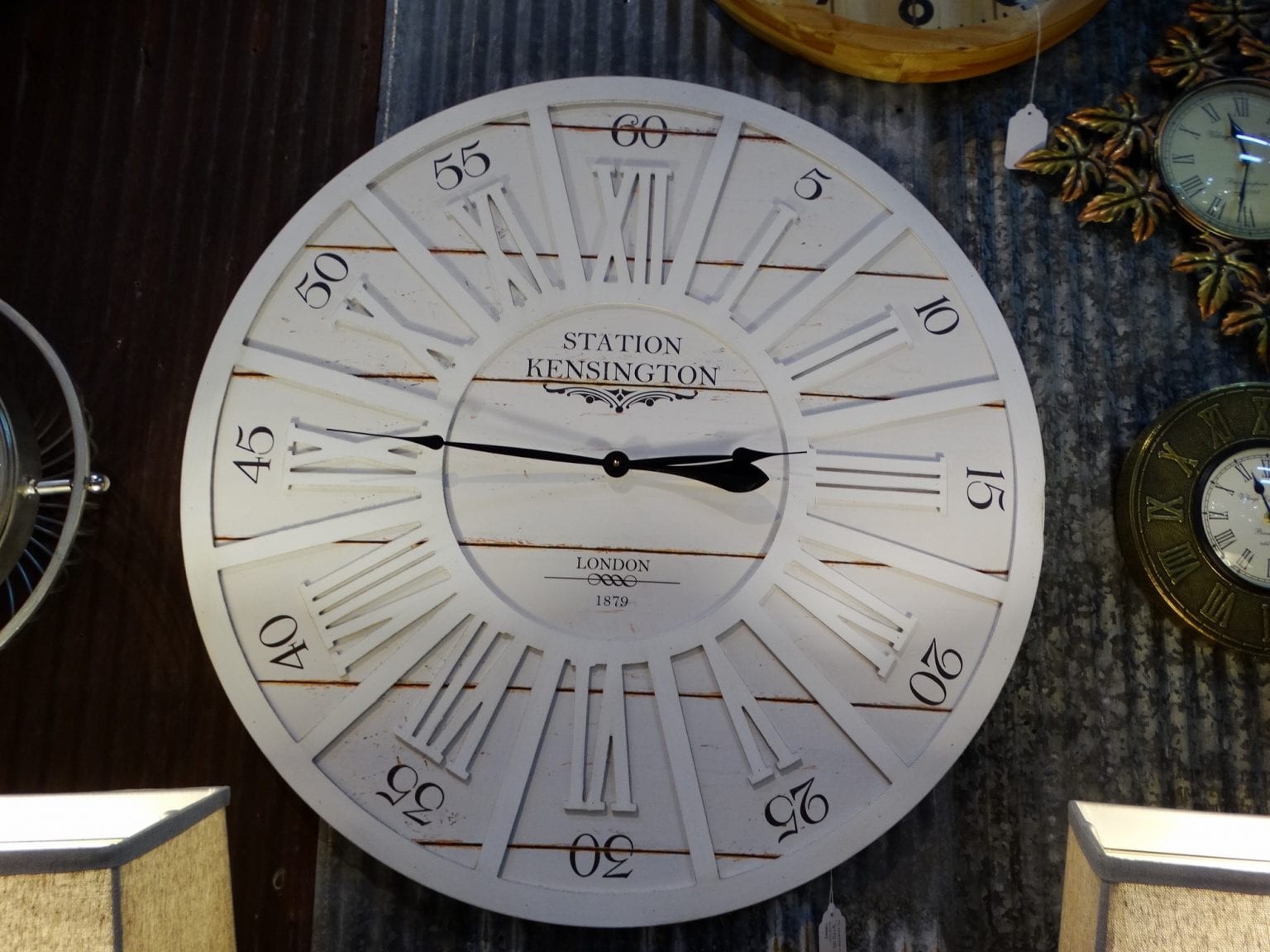 Round Wall Clock features white roman numerals on white rustic wood.