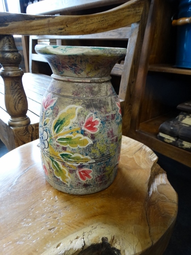 Decorative ceramic vase with a colorful floral design on a weathered surface, placed on a round wooden table in a rustic room.