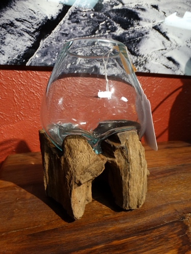 Glass bowl balanced on weathered driftwood sculpture on a wooden table, with a hanging tag.