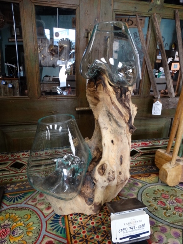 Rustic wooden base with two glass lamp shades set on a colorful patterned table in a shop window.