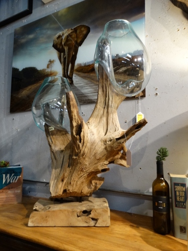 Decorative driftwood sculpture with two glass bulb forms mounted on a wooden base in a shop display.