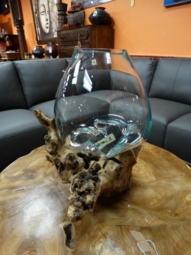 Decorative glass fishbowl resting on a carved driftwood centerpiece on a wooden coffee table in a showroom.